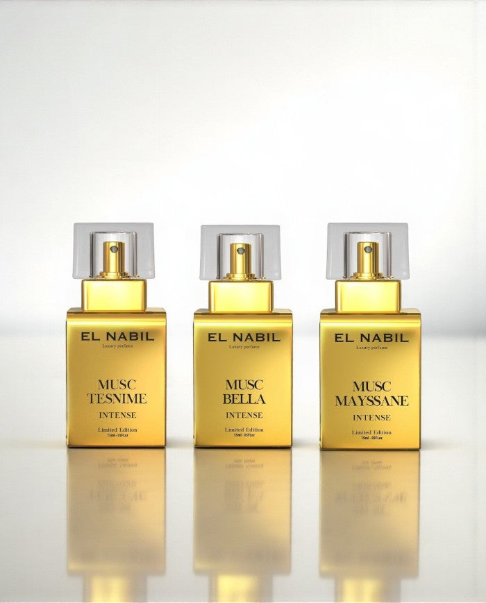 Pack 3 Eaux de Parfum Intense El Nabil 15 ml – Musc Bella, Musc Mayssane, Musc Tesnime, flacons or alignés avec pétales et fleurs colorées, reflet sur surface brillante.